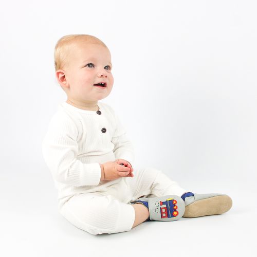 Small boy sitting on floor wearing pale grey Dotty Fish train shoes.