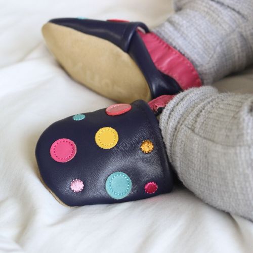 Baby wearing navy leather shoes with colourful dots.