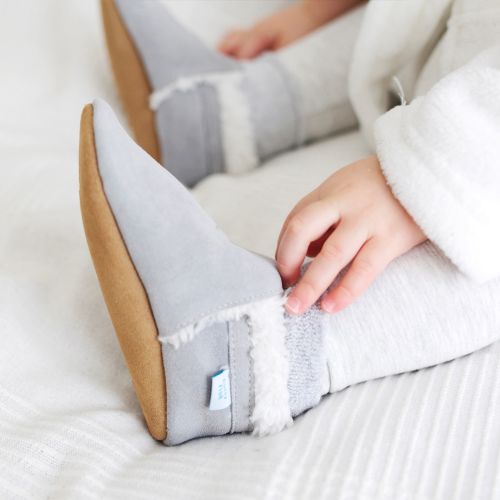 Baby lying on bed, wearing light grey suede Dotty Fish barefoot slippers, with fleece lining.