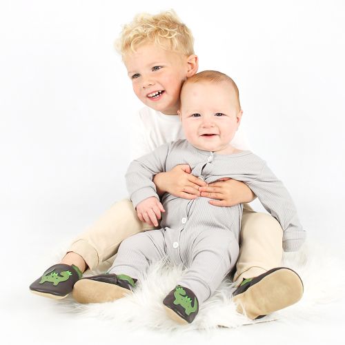 A baby and toddler sitting together wearing brown Dotty Fish dinosaur shoes.