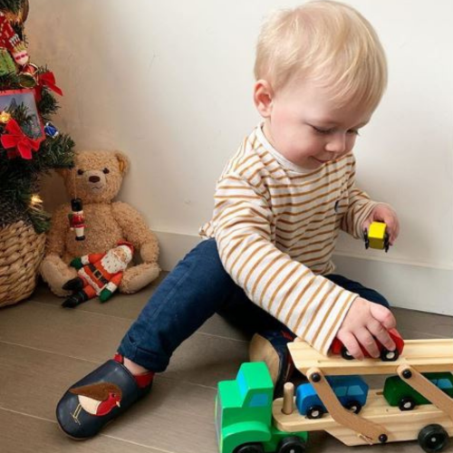 Infant boy sitting, wearing navy blue Dotty Fish shoes with brown and red robin design, playing with toys.