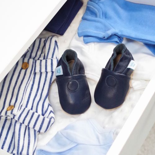 Plain navy leather baby shoes in drawer with baby clothing.