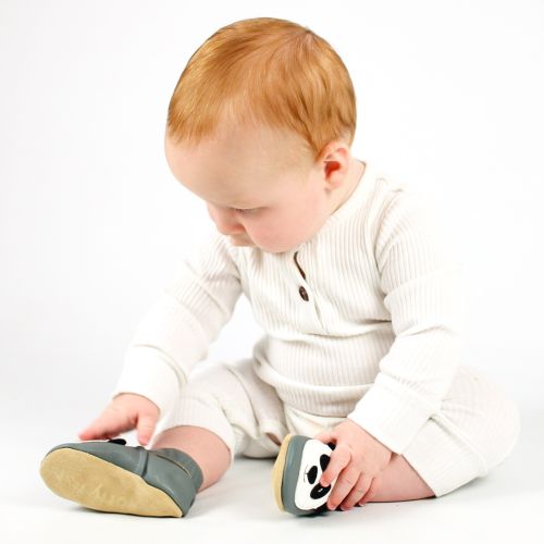 Baby boy sitting on floor, wearing grey Dotty Fish shoes with white and black panda design, looking at his feet.