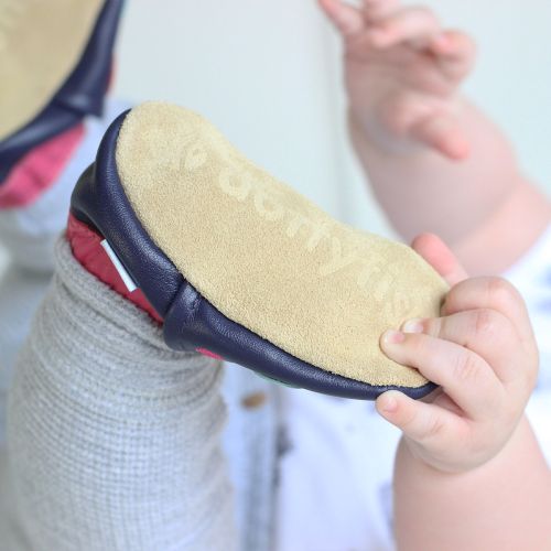 Baby wearing navy Dotty Fish barefoot shoes with pink ankle trim and multicoloured spots.