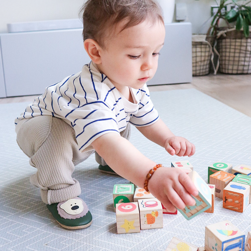 Toddler playing with toys, wearing Dotty Fish leather shoes with bear design.