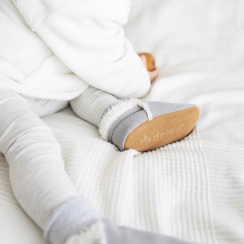 Toddler wearing pale grey suede slippers with fleece lining.