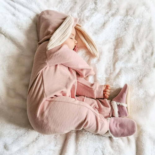 Baby in pink suede slippers, wearing bunny onesie.