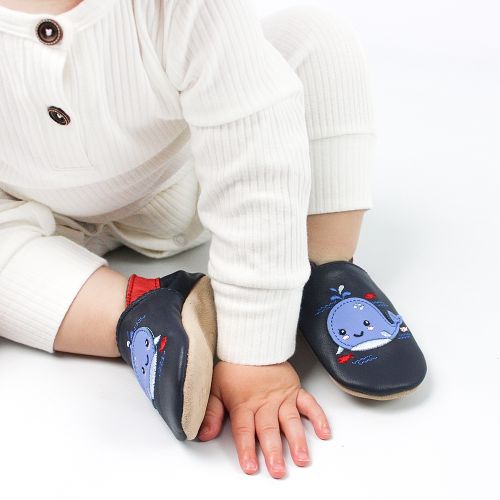 Baby boy sitting, wearing navy Dotty Fish barefoot shoes with blue whale design.