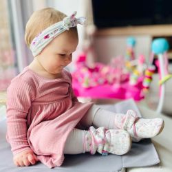 Toddler girl sitting wearing cream cotton booties with floral design.