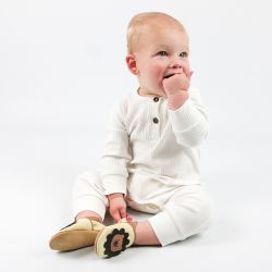 Baby wearing cream Dotty Fish shoes with lion design and white baby grow, sitting on floor.