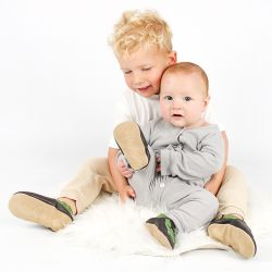  A baby and toddler sitting together wearing brown Dotty Fish dinosaur shoes.