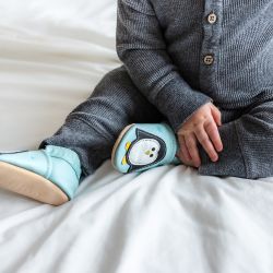 Baby boy sitting on bed, wearing mint green Dotty Fish shoes with white and black penguin design.
