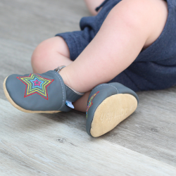 Toddler wearing grey leather Dotty Fish first walker shoes with embroidered rainbow star design.
