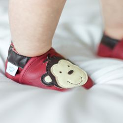 Toddler wearing red Dotty Fish shoes with brown and cream monkey design.