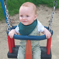 Baby on swing wearing Dotty Fish dark green cotton bandana bib.