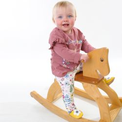 Toddler girl wearing yellow Dotty Fish barefoot shoes with grey ankle trim and white flower design, sitting on rocking horse.