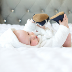 Baby lying on bed, wearing navy suede slippers.