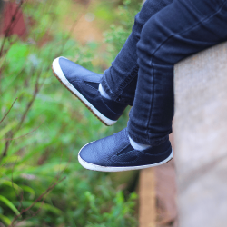 Boy wearing unisex first walker slip-on shoes in charcoal leather with rubber sole.