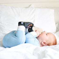 Baby boy lying on bed, wearing charcoal Dotty Fish shoes with silver space rocket design.