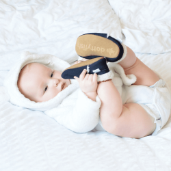 Baby lying on bed, wearing navy suede Dotty Fish barefoot slippers, with fleece lining.