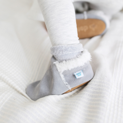 Small child standing on bed, wearing Dotty Fish grey suede slippers.