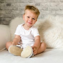 Toddler boy sitting down, wearing grey suede Dotty Fish children’s slippers.