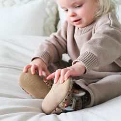 Toddler girl wearing woodland booties, sitting on bed.