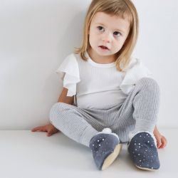 Toddler girl sitting, wearing dark grey with silver stars suede Dotty Fish children’s slippers.