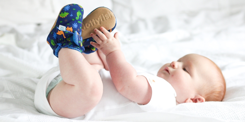 Baby lying on bed, wearing Dotty Fish navy cotton booties with dinosaur pattern.